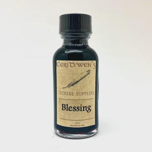 May include: A small clear glass bottle filled with dark liquid, topped with a black screw cap. The label reads Ceridwen's Scribe Supplies, Blessing, and 1 fl oz external use only, featuring a graphic illustration of a quill pen.