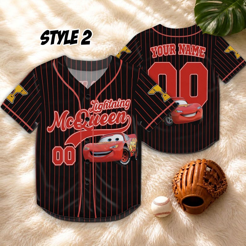 Puede incluir: Camiseta de b&eacute;isbol negra con finas rayas rojas, con gr&aacute;ficos de Lightning McQueen y el n&uacute;mero 00. La camiseta tiene el texto "STYLE 2" en la parte superior izquierda. Un guante y una pelota de b&eacute;isbol est&aacute;n en primer plano.