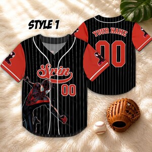 May include: Black and red baseball jersey with white pinstripes, featuring a Spider-Man graphic and the word "Spin". The jersey has red sleeves and the number "00". A baseball glove and ball are also visible.