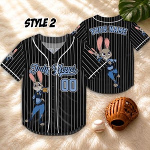 May include: Black baseball jersey with white pinstripes, featuring the character Judy Hopps from Zootopia. The jersey has the name "Judy Hopps" and the number "00" on the front. The back of the jersey has the text "YOUR NAME". A baseball glove and ball are in the image.