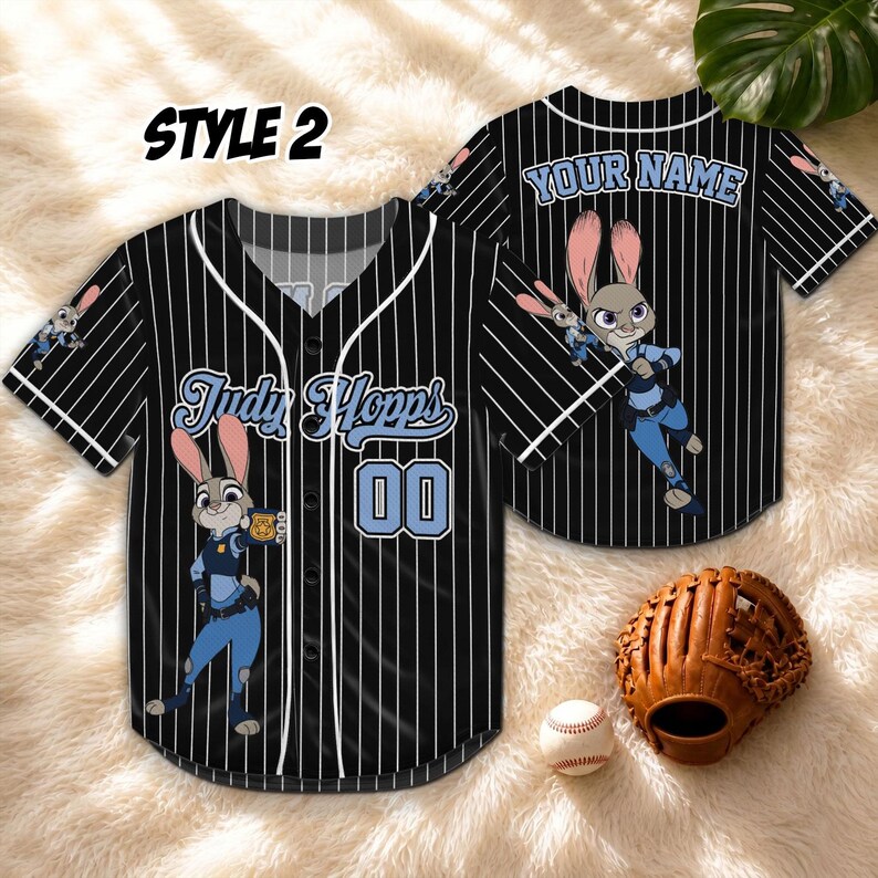 May include: Black baseball jersey with white pinstripes, featuring the character Judy Hopps from Zootopia. The jersey has the name "Judy Hopps" and the number "00" on the front. The back of the jersey has the text "YOUR NAME". A baseball glove and ball are in the image.