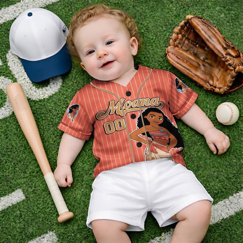 Może przedstawiać: Niemowlę w czerwono-białej koszulce baseballowej z napisem "Moana" i numerem "00". Koszulka jest połączona z białymi szortami. Na zdjęciu znajdują się r&oacute;wnież kij baseballowy, rękawica, piłka i biało-niebieska czapka.
