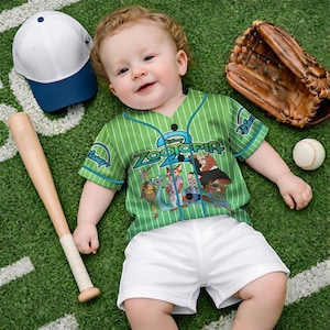 May include: A baby wearing a green baseball jersey with the text "Zootopia 2" and Disney logos, paired with white shorts. Accessories include a baseball bat, a white and blue baseball cap, a baseball glove, and a baseball. The scene is set on a green field.