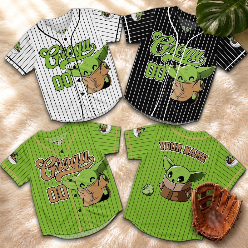 May include: Four baseball jerseys featuring Grogu graphics. The jerseys are white with black pinstripes, black with white pinstripes, and green with green pinstripes. One green jersey has a baseball glove. The jerseys have the number 00.
