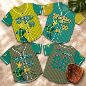 Puede incluir: Cuatro camisetas de b&eacute;isbol en tonos verdes y amarillos, con el personaje "Electro" y el n&uacute;mero "00". Las camisetas tienen mangas cortas y una parte delantera abotonada. Tambi&eacute;n se ve un guante de b&eacute;isbol marr&oacute;n.
