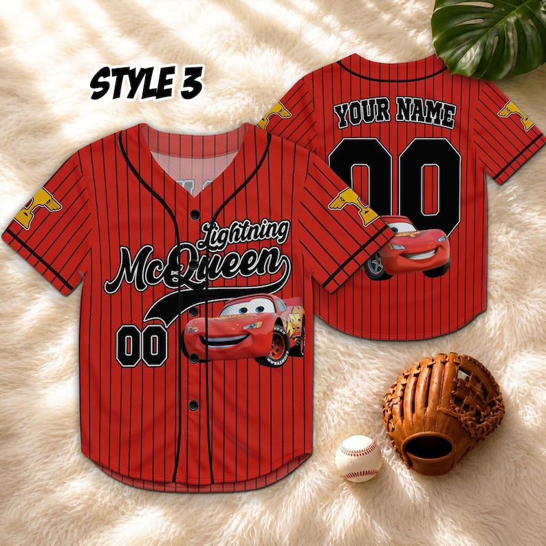 Puede incluir: Camiseta de b&eacute;isbol roja con finas rayas negras, con gr&aacute;ficos de Lightning McQueen y el n&uacute;mero 00. La camiseta tiene el texto "Your Name" en la espalda. Un guante y una pelota de b&eacute;isbol tambi&eacute;n est&aacute;n en la imagen.
