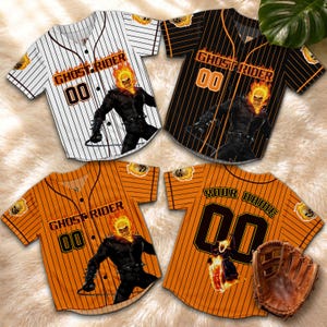 Op de afbeelding: Vier honkbalshirts met de Ghost Rider-afbeelding. De shirts zijn wit met zwarte krijtstrepen, zwart met oranje krijtstrepen en oranje met zwarte krijtstrepen. E&eacute;n shirt heeft een honkbalhandschoen.