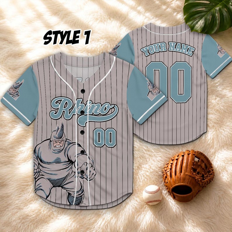 May include: Grey baseball jersey with blue sleeves and pinstripes, featuring the word "Rhino" and the number "00". The jersey has a cartoon illustration of a rhino character. The text "STYLE 1" is at the top. A baseball glove and ball are also in the image.