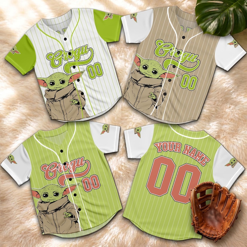 K&ouml;nnte beinhalten: Baseball-Trikots mit einem Grogu-Motiv und der Nummer 00. Die Trikots sind in Wei&szlig;, Beige und Gr&uuml;n gehalten und zeigen das Bild von Grogu auf der Vorderseite. Ein Trikot hat "Your Name" auf dem R&uuml;cken. Ein brauner Baseballhandschuh ist ebenfalls zu sehen.