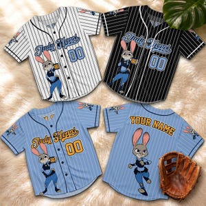 May include: Four baseball jerseys with a cartoon character design. Two jerseys are white with black pinstripes, and two are light blue with white pinstripes. Each jersey features the name "Judy Hopps" and the number "00". A baseball glove is also visible.