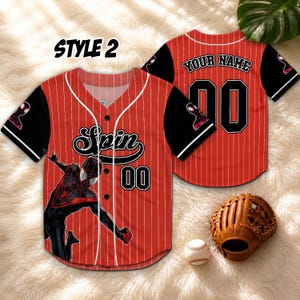 May include: Red and white pinstripe baseball jersey with black sleeves. The jersey features a Spider-Man graphic, the word "Spin", and the number "00". The back of the jersey has the text "YOUR NAME" above the number "00". A baseball glove and ball are also in the image.