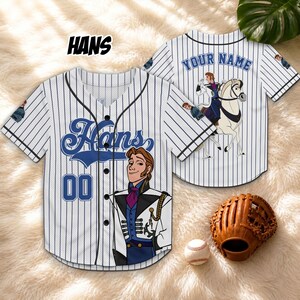 以下が含まれることがあります： 白と黒のピンストライプの野球ジャージ。青いスクリプトで「Hans」という名前と「00」の数字が入っています。ジャージにはキャラクターの漫画イラストが描かれています。野球とグローブが前景にあります。
