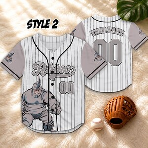 May include: A white and black pinstripe baseball jersey with the word "Rhino" and the number "00" on the front. The jersey features a cartoon illustration of a rhino. The back of the jersey has the number "00" and the text "YOUR NAME".