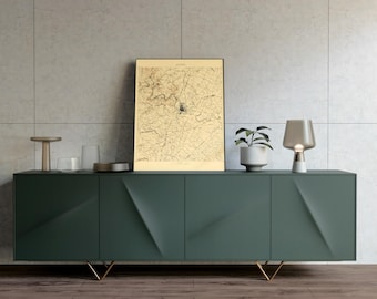 May include: A dark green modern sideboard with gold legs, holding a framed vintage map, a small potted plant, a table lamp, and decorative items. The cabinet has a geometric design on the doors.