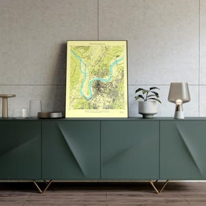 Może przedstawiać: Oprawiona mapa Chattanooga, Tennessee, z jasnozieloną i niebieską kolorystyką, eksponowana na ciemnozielonej szafce. Szafka ma złote nogi i jest ozdobiona małą rośliną, lampą i dekoracyjnymi szklanymi przedmiotami.