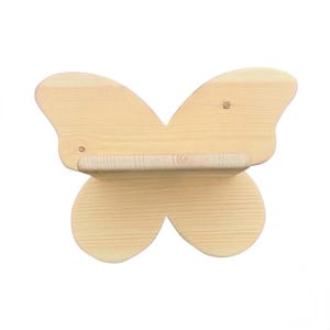 Pode incluir: Uma prateleira de parede de madeira de cor clara em forma de borboleta. A prateleira apresenta uma superfície plana horizontal fixada no centro do painel traseiro em forma de borboleta, que exibe um padrão de grão de madeira natural e nós visíveis.