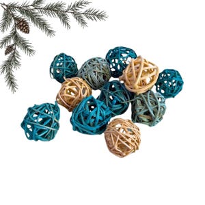 Pode incluir: Um conjunto de esferas decorativas feitas de fibras naturais entrelaçadas, apresentando uma paleta de cores em tons de azul-petróleo, azul-claro e bege natural. Um pequeno ramo de folha perene com uma pinha está no canto superior esquerdo.