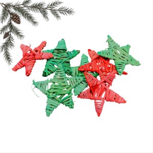 Pode incluir: Uma coleção de ornamentos em forma de estrela feitos de material trançado, com uma paleta de cores vibrantes em vermelho e verde. As estrelas estão dispostas em um grupo, algumas sobrepostas, e acompanhadas por um ramo de pinheiro.