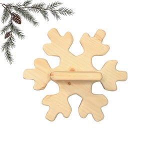 Pode incluir: Uma prateleira de madeira de cor clara em forma de floco de neve com uma barra horizontal no centro. O grão natural da madeira é visível em toda a peça, que apresenta seis braços simétricos e um acabamento lixado suave para uma aparência limpa.