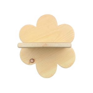 Pode incluir: Uma prateleira de parede de madeira de cor clara em forma de flor de seis pétalas. A prateleira apresenta uma superfície plana horizontal que se estende pelo centro da silhueta floral, exibindo um padrão de grão de madeira natural com um nó visível.