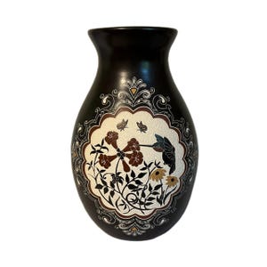May include: A dark brown ceramic vase with a decorative floral and hummingbird design. The vase features a central oval panel with brown flowers, butterflies, and a hummingbird, framed by an ornate border.