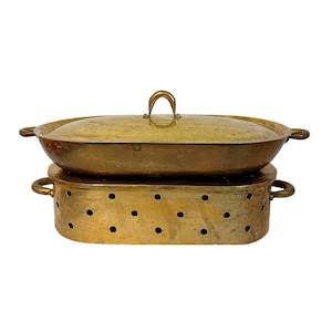 May include: A vintage brass food warmer with a lid and a perforated base. The oval-shaped warmer has handles on the sides and a loop handle on the lid. The brass has a warm, aged patina, suggesting its use over time.
