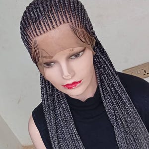 Peut inclure: Perruque tressée grise et noire, présentée sur une tête de mannequin. La perruque est dotée d'un devant en dentelle et d'une finition de qualité. Les tresses sont disposées avec soin, créant un look élégant et moderne. Le mannequin porte un haut noir.