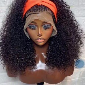 Puede incluir: Una cabeza de maniquí de piel oscura que muestra una peluca negra rizada con una diadema naranja. La peluca tiene una parte delantera de encaje y está peinada con rizos voluminosos. El maniquí tiene maquillaje aplicado, incluyendo sombra de ojos y lápiz labial.