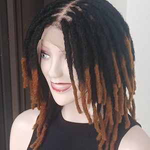 May include: A black and brown dreadlock wig on a mannequin. The wig features a lace front and a mix of black and brown dreadlocks. The dreadlocks are long and hang down, with the ends of the dreadlocks dyed brown.