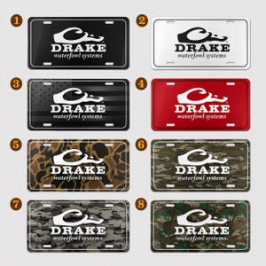May include: A collection of license plates with the "DRAKE waterfowl systems" logo. The plates feature various designs, including solid black, white, red, camouflage, and a design with American flag stripes.