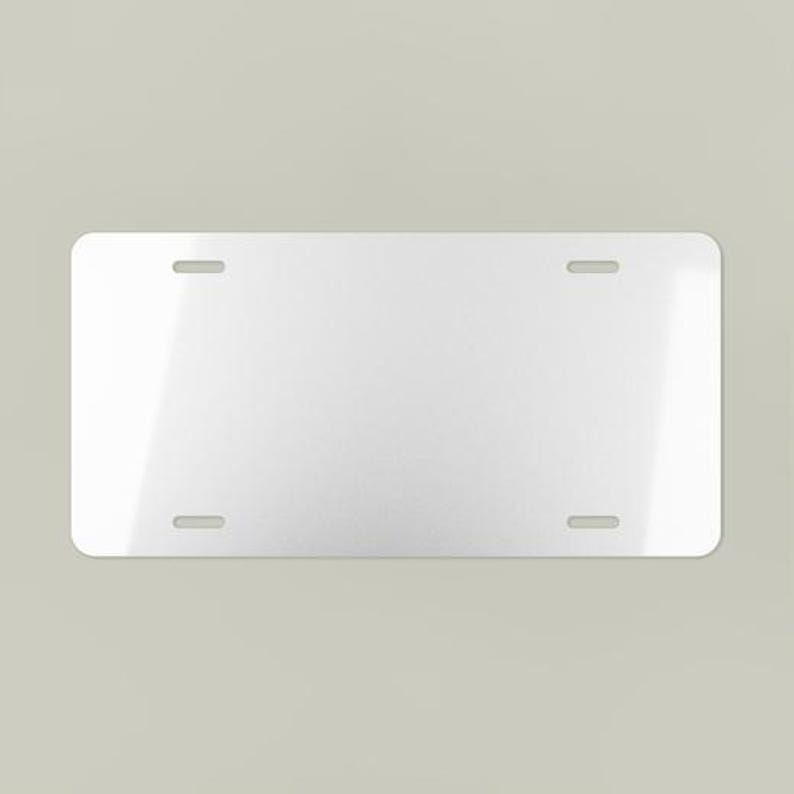 May include: A blank, rectangular license plate with rounded corners. The plate is white with four evenly spaced mounting holes. The surface has a slight sheen, reflecting ambient light.