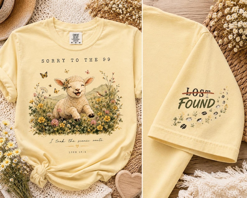 May include: A pale yellow t-shirt featuring a graphic of a smiling lamb in a field of wildflowers with butterflies. The text reads SORRY TO THE 99, I took the scenic route, and LUKE 15:4. The sleeve displays the text LOST FOUND with small hoof prints.