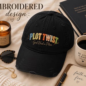 Puede incluir: Una gorra de béisbol negra con visera desgastada que presenta el texto bordado PLOT TWIST en letras estampadas multicolores y la frase God Had a Plan en una fuente cursiva centrada en el panel frontal de la gorra.