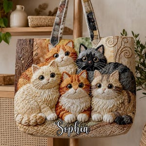 May include: A beige tote bag with a tapestry design of six cats in shades of orange, black, and cream. The bag has patterned handles and the name "Sophia" is embroidered on the bottom. The bag is suitable for carrying items.