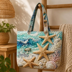 May include: A quilted tote bag depicting a beach scene with starfish, seashells, and coral. The bag features blue and white waves, sand, and the name "Sophia" in script. The handles and top have a seashell pattern.
