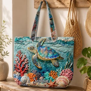 May include: A quilted tote bag with a sea turtle design, coral, and seashells in shades of blue, teal, orange, and red. The name "Sophia" is printed on the front. The bag's handles are patterned with marine life. The bag is designed for carrying items.