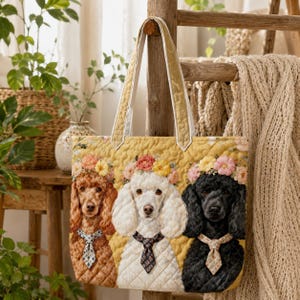 May include: A quilted tote bag featuring three poodle portraits in brown, white, and black, each adorned with a floral crown and a patterned tie. The bag has a yellow background and white handles.