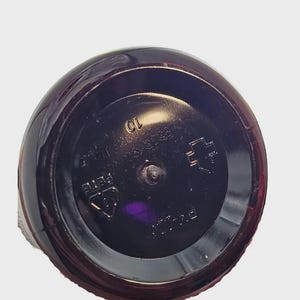 May include: Close-up of the base of a dark brown plastic bottle. The circular base has embossed markings, including the number "10" and the letters "PETE". The bottle's surface reflects light, highlighting its shape.