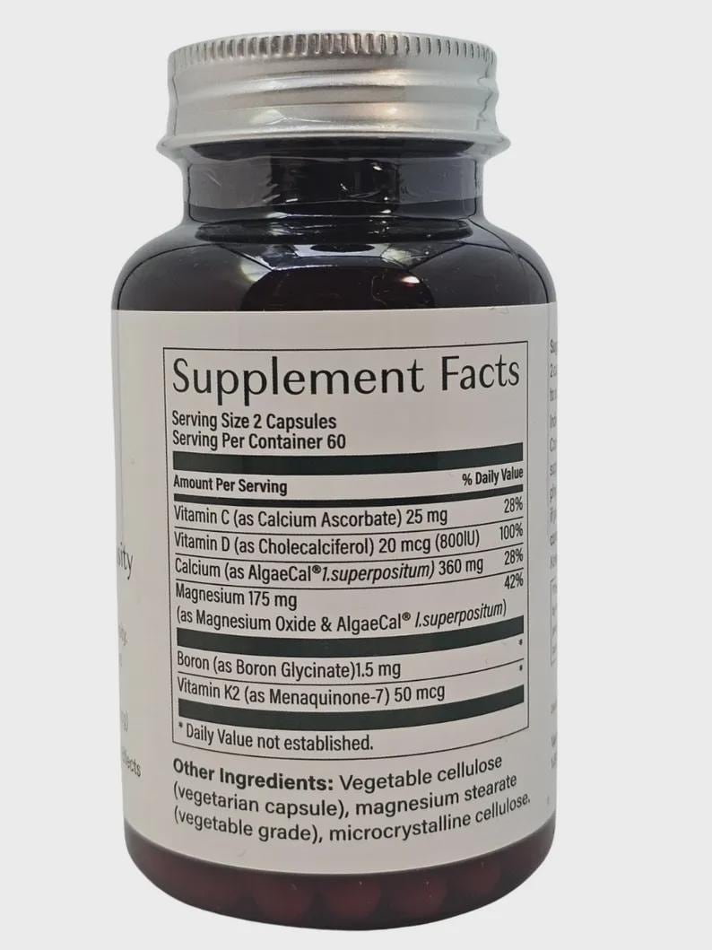 May include: A dark brown supplement bottle with a silver lid. The label displays "Supplement Facts" and lists ingredients like Vitamin C, D, and K2. The bottle contains 60 servings of 2 capsules each.