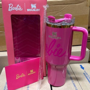 May include: A pink Stanley tumbler with a handle, featuring the Barbie logo. The tumbler has a clear lid and a clear straw. The box and card also feature the Barbie and Stanley logos.