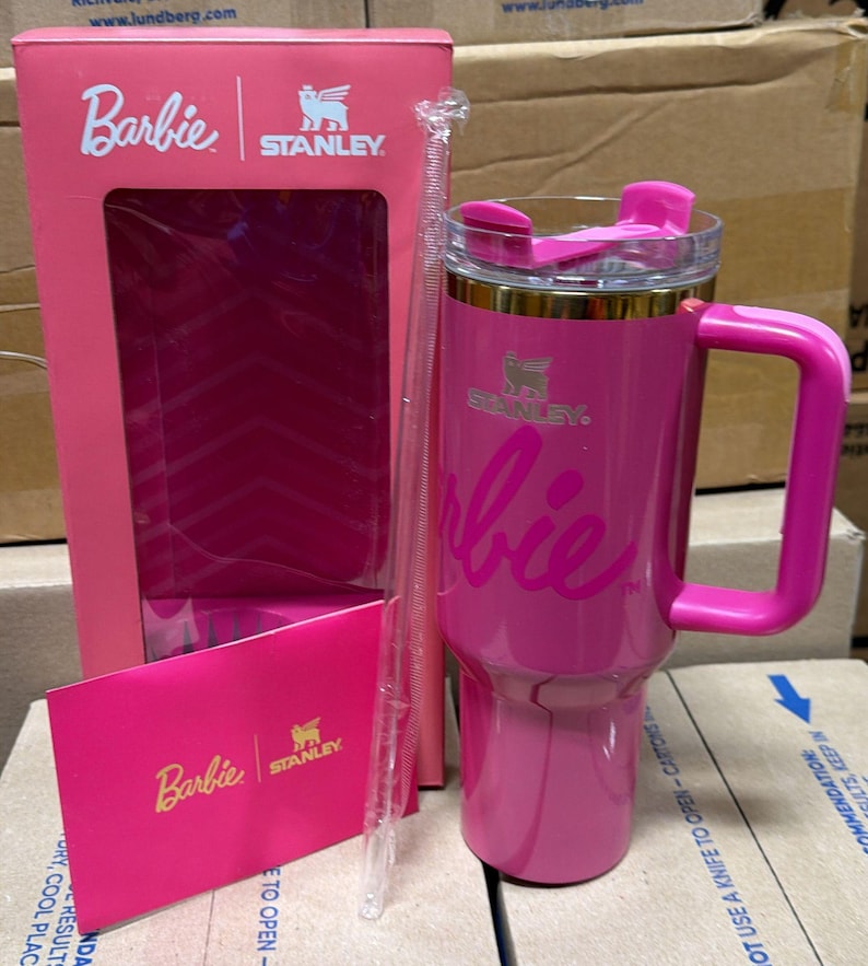 May include: A pink Stanley tumbler with a handle, featuring the Barbie logo. The tumbler has a clear lid and a clear straw. The box and card also feature the Barbie and Stanley logos.