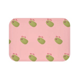 Puede incluir: Una alfombra de baño rectangular con un patrón repetido de aceitunas verdes con corazones rosas y el texto "Olive You" sobre un fondo rosa claro. La alfombra tiene esquinas redondeadas.