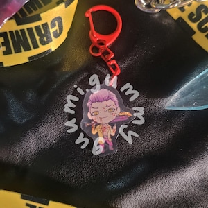 May include: A red keychain with a cartoon character charm. The charm features a character with purple hair, holding a tray with food. The keychain is attached to a yellow and black crime scene tape.