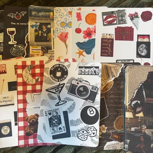 May include: A collection of decorative stickers and images, including a bat, a wine glass, a newspaper clipping, a flower, a camera, and a playing card. The stickers are arranged on a green surface.