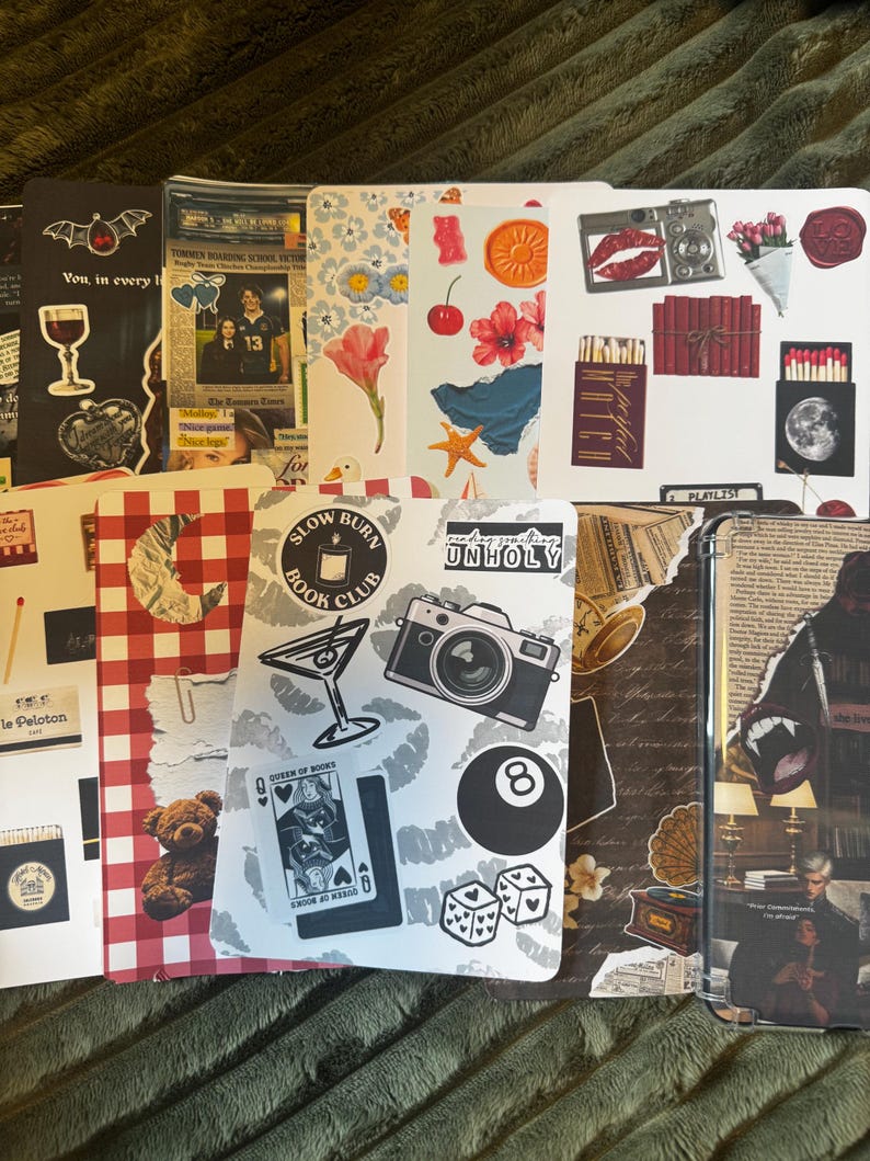 May include: A collection of decorative stickers and images, including a bat, a wine glass, a newspaper clipping, a flower, a camera, and a playing card. The stickers are arranged on a green surface.