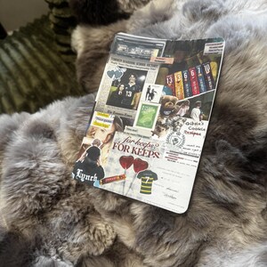 May include: A plush, faux fur blanket in shades of gray and brown. A decorative card with the text "TOMMEN BOARDING SCHOOL VICTORY" and "for keeps? FOR KEEPS" is on top of the blanket. The card also features images and text.