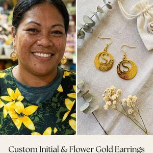 May include: Gold-colored earrings with the letter "S" and floral details. The earrings are shown on a person and also displayed on a neutral surface with a small bag and sprigs of greenery. The text reads "Custom Initial & Flower Gold Earrings."