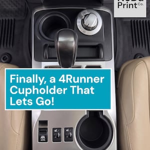 May include: Interior view of a car's center console, featuring a cup holder, gear shift, and control knobs. The text "Finally, a 4Runner Cupholder That Lets Go!" is displayed on a blue background. The logo "NoDa Print Co." is in the upper right corner.
