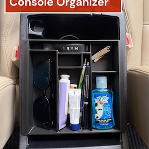 May include: Black center console organizer for a 4Runner. The organizer is filled with sunglasses, pens, hand sanitizer, and other small items. The text "4Runner Center Console Organizer" is displayed in a red rectangle.