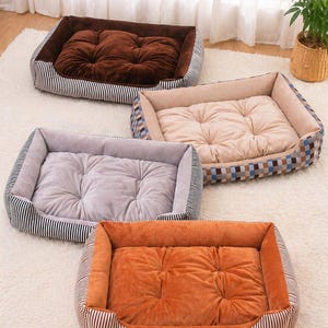 Puede incluir: Cuatro camas rectangulares para mascotas en marrón, beige, gris y naranja. Cada cama tiene un cojín central afelpado y un borde a rayas o estampado. Las camas están diseñadas para la comodidad y son adecuadas para mascotas pequeñas y medianas.